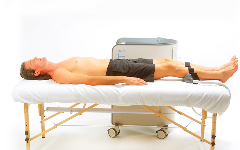 Male patient lying in the clinic's bed with calves getting EMSCULPT NEO® Treatment